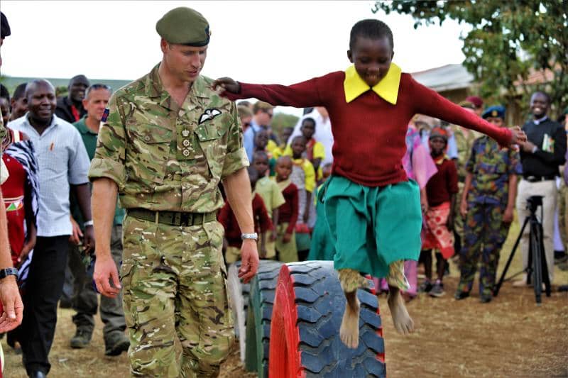 Prince William in army uniform watching a young boy playing and jumping from a tire