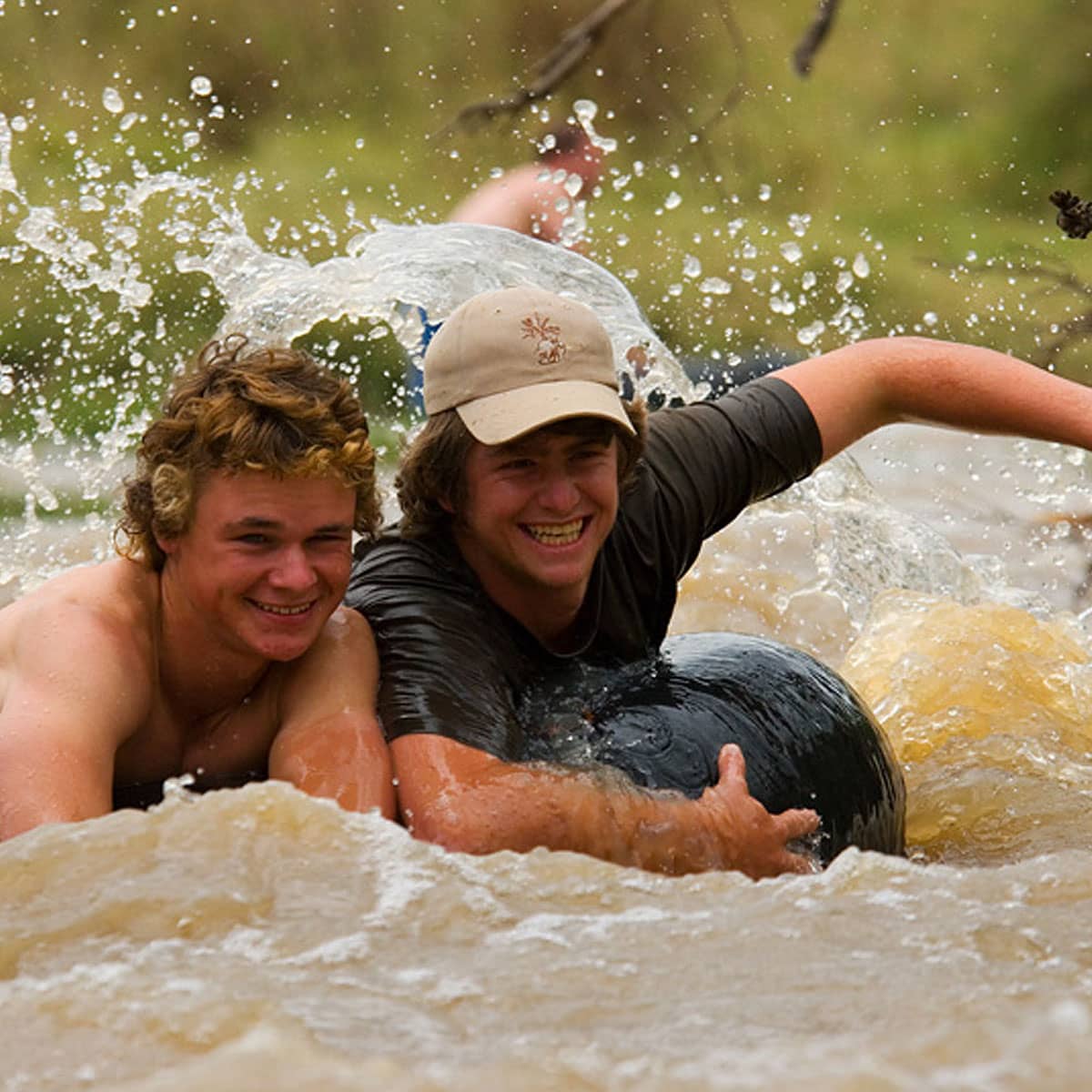 2 young men tubing; holding onto a rubber ring whilst splashing down the river